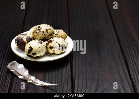 Wachteleier auf weißer Untertasse. Vogelfeder auf dem Tisch. Dunkler Holzhintergrund. Draufsicht. Kopierbereich Stockfoto