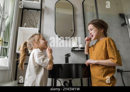 Zwei Schwestern putzen sich im Badezimmer die Zähne. Sie stehen nebeneinander und lächeln Stockfoto