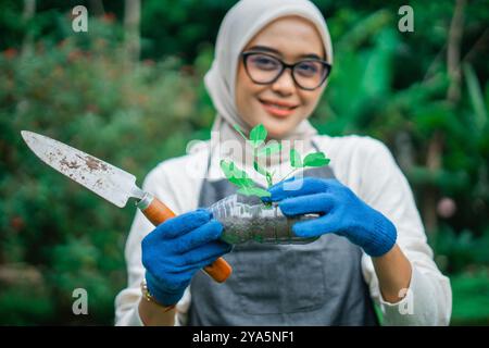 Hijab-Frau mit grünem Setzling in wiederverwendeter Plastikflasche Stockfoto