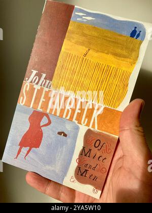 Das Cover der Taschenbuch-Novelle „of Mäuse and Men“ von John Steinbeck in der Hand eines Mannes Stockfoto