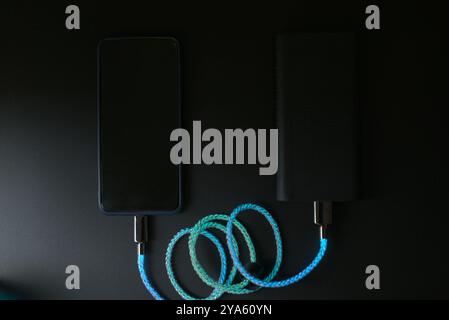 Smartphone lädt über eine Powerbank mit LEDs auf schwarzem Hintergrund Stockfoto