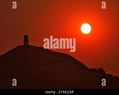 Blutmond, der über dem St Michael's Tower am Glastonbury Tor auf den Somerset Levels UK aufsteigt, verursacht durch dicken Nebel am Horizont Stockfoto