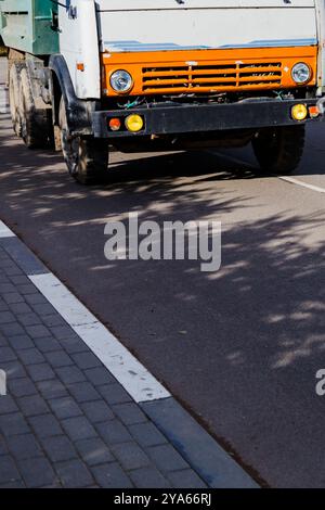 Ein orange-weißer Lkw, der seine leuchtenden Farben zeigt, fährt eine geschäftige Straße hinunter und navigiert mühelos durch den Morgenverkehr Stockfoto