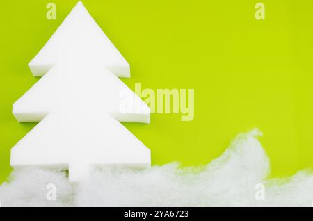 Ein weißer Styroporbaum hebt sich vor einem leuchtend grünen Hintergrund deutlich hervor und erzeugt einen auffälligen visuellen Kontrast, der festlich und schön wirkt Stockfoto
