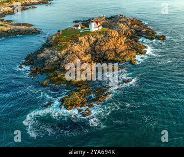 Ein Leuchtturm steht auf einer felsigen Insel, umgeben vom blauen Meer, mit Wellen, die sanft gegen die Felsen stürzen. Die Szene fängt das friedliche und ist ein Stockfoto