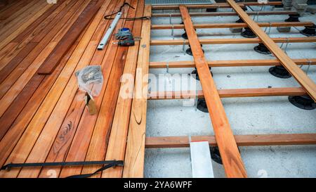 Ein teilweise gebautes Holzdeck mit Werkzeugen und Materialien verstreut. Holzbalken und Balken sind über Stützen gelegt, die die Unterkonstruktion des Decks zeigen Stockfoto