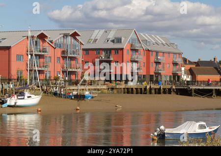 Teil der Uferpromenade des Flusses Colne bei Ebbe bei Wivenhoe in Essex mit farbenfrohen Wohnungen mit Blick auf den Fluss und den Bootssteg. Stockfoto