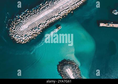 Ein Fischerboot, das in die Mole eines Seehafens einfährt, mit Blick von oben von einer Drohne Stockfoto