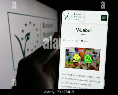 Person, die ein Smartphone hält und auf dem Bildschirm die Webseite der Organisation European Vegetarian Union (EVU) mit Logo angezeigt wird. Konzentrieren Sie sich auf die Mitte des Telefondisplays. Stockfoto