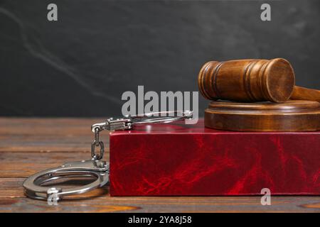 Buch, richterlicher Hammer und Handschellen auf Holztisch vor grauem Hintergrund, Platz für Text Stockfoto