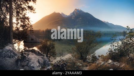 Majestätische Berge in den deutschen Alpen spiegeln sich bei Sonnenaufgang in einem malerischen See. Idyllische Panoramalandschaft in Blau- und Goldtönen Stockfoto