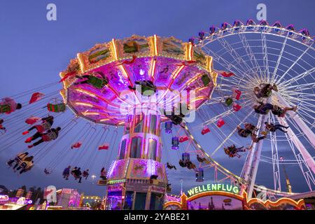 Ein lebhafter Jahrmarkt in der Abenddämmerung, beleuchtet von einem großen Riesenrad und einem bunten Kettenkarussell, Cannstadter Volksfest, Stuttgart-Bad Cannstadt, Baden-Wi¿½ Stockfoto