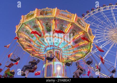 Beleuchtetes Karussell und Riesenrad bei Nacht in einem belebten Vergnügungspark, Jahrmarkt, Wellenflug, Cannstadter Volksfest, Stuttgart-Bad Cannstsdt, Baden Stockfoto