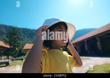 Ein Kind genießt fröhlich einen sonnigen Tag im Freien in einem gelben T-Shirt und einem weißen Hut Stockfoto