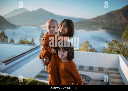 Drei Kinder in leuchtenden Orange-Outfits mit wunderschönem Bergblick Stockfoto
