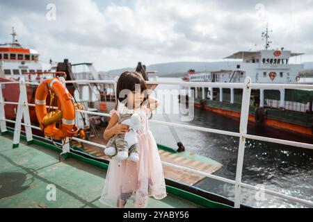 Ein Kind mit einer geliebten Puppe macht eine Fahrt mit der Fähre zwischen farbenfrohen Booten in einem Hafen Stockfoto