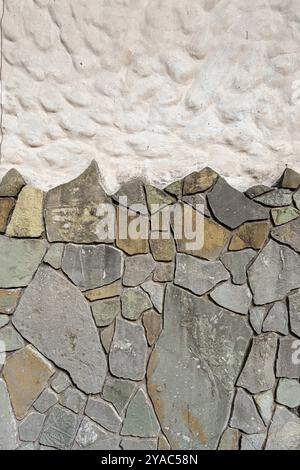 Eine Wand aus Stein und weißem Putz. Die Wand besteht aus vielen kleinen Steinen, was ihr ein raues und ungleichmäßiges Aussehen verleiht. Stockfoto