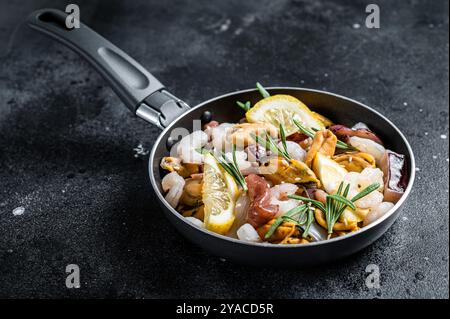 Roher Mix Meeresfrüchte-Cocktail mit Garnelen, Garnelen, Muscheln, Tintenfischen und Tintenfischen in einer Pfanne bereit zum Kochen. Schwarzer Hintergrund. Draufsicht. Stockfoto