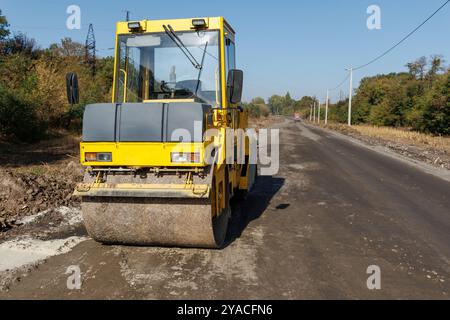 Auf der Straße steht eine gelbe Asphaltbahn. Eine Eisbahn zum Pflastern und Verdichten von Böden, zum Verlegen von Asphalt oder Sand bei Straßenreparaturen oder Bauarbeiten Stockfoto