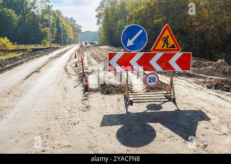 In Bearbeitung. Baustellen, Straßenschilder. Männer bei der Arbeit. Einige Schilder für laufende Arbeiten auf der Stadtstraße. Schranken und Straßenschilder. Silhouette von Stockfoto