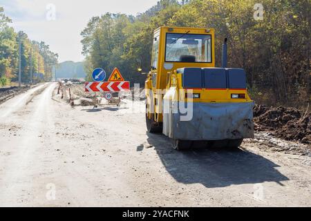 Eine gelbe Rollbahn, die auf einer teilweise fertiggestellten Straße geparkt ist. Eine Eislaufbahn zum Verlegen von Asphalt oder Sand bei Straßenreparaturen oder Bauarbeiten. Straßenreparatur Stockfoto