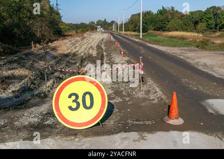 Eine im Bau befindliche Straße mit einem großen gelben kreisförmigen Geschwindigkeitsbegrenzungsschild von 30 km/h die Baustelle ist mit rot-weiß gestreiftem Hahn markiert Stockfoto