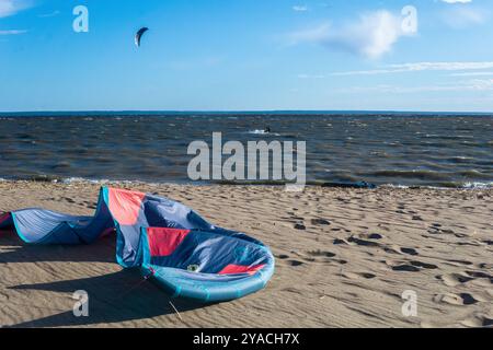 Kotlin, Russland - 20. Juni 2024: Zugdrachen liegt am Ufer, ein Kiteboarder ist im Meer sichtbar, der von einem anderen Power-KI über das Wasser gezogen wird Stockfoto