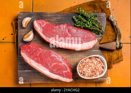 Cap Rump Steak, rohes Rindfleisch Steak mit Thymian und Salz auf Holzbrettern. Orangefarbener Hintergrund. Draufsicht. Stockfoto