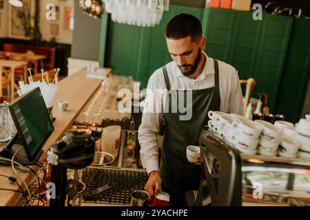 In einem warmen und einladenden Café gießt ein engagierter Barista fachmännisch Milch in eine Kaffeetasse und sorgt so für ein angenehmes Erlebnis für Gäste. Stockfoto