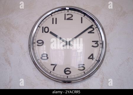 Eine große Uhr mit schwarzem Zifferblatt an der Wand. Große weiße Wanduhr mit Zeigern und Zahlen. Stockfoto