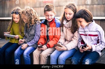 Kinder, die auf der Straßenbank im Park auf Smartphones spielen Stockfoto