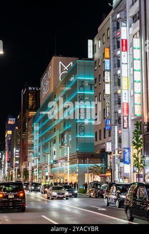 Ginza ist mit Taxis und Autos beschäftigt, die nachts vor der grünen beleuchteten Fassade des Matsuya- und Tiffany-Ginza-Gebäudes fahren. Andere Gebäude. Stockfoto