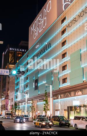 Das Wahrzeichen von Matsuya Ginza und Tiffany Store Gebäude beleuchtet in blauem, grünem, diffusem Licht. Vor der Straße fahren Autos und Taxis vorbei. Stockfoto