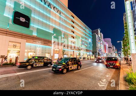 Blick entlang der Ginza mit dem Wahrzeichen Matsuya Ginza und dem Tiffany Store Gebäude beleuchtet in blauem, grünem, diffusem Licht. Taxis fahren auf der Straße. Stockfoto