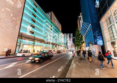 Ginza in der Nacht mit dem Matsuya Ginza und Tiffany Store Gebäude beleuchtet in blauem, grünem Licht. Leute, die auf dem Gehweg spazieren. Stockfoto