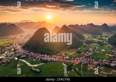 Blick aus der Vogelperspektive auf den goldenen Sonnenuntergang über dem Bac Son Valley mit Bergen, üppigen grünen Feldern, gewundenen Fluss und Vorstadtdorf in lang Son, Vie Stockfoto