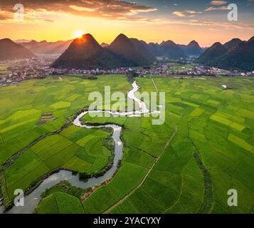 Blick aus der Vogelperspektive auf den farbenfrohen Sonnenuntergang über dem Bac Son Valley mit Bergen, üppigen grünen Feldern, gewundenen Fluss und Vorstadtdorf auf dem Land bei lang so Stockfoto