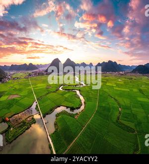 Blick aus der Vogelperspektive auf den farbenfrohen Sonnenuntergang über dem Bac Son Valley mit Bergen, üppigen grünen Feldern, gewundenen Fluss und Vorstadtdorf auf dem Land bei lang so Stockfoto