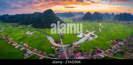 Blick aus der Vogelperspektive auf den farbenfrohen Sonnenuntergang über dem Bac Son Valley mit Bergen, üppigen grünen Feldern, gewundenen Fluss und Vorstadtdorf auf dem Land bei lang so Stockfoto