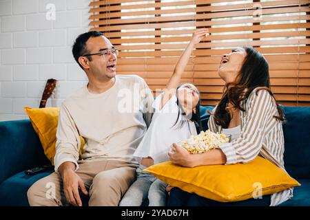 Eine glückliche Familie voller Freude schaut fern, während sie auf einem modernen Sofa zu Hause Popcorn isst Stockfoto