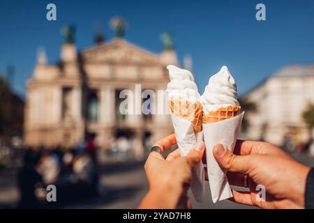 Nahaufnahme von zwei Eiskegeln in Paaren Händen. Die Leute essen im Freien Street Food und genießen die Lwiwer Architektur Stockfoto