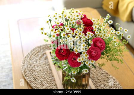 Wunderschöne Ranunkelblumen und Kamillen in Vase auf dem Tisch drinnen Stockfoto