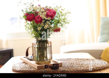 Wunderschöne Ranunkelblumen und Kamillen in Vase auf dem Tisch drinnen Stockfoto