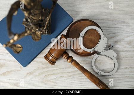 Handschellen, richterlicher Hammer, Lady Justice Figur und Buch auf weißem Holztisch, flach Stockfoto