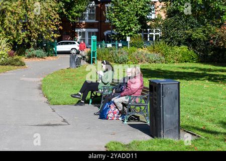 Leute sitzen auf Parkbänken im Queens Park loughborough Stockfoto