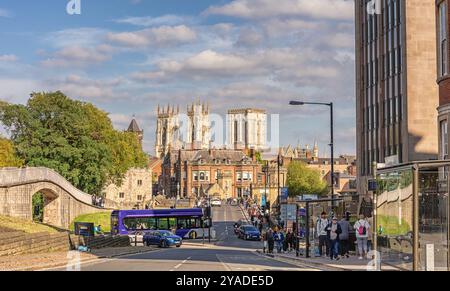 Ein Blick auf die Straße hinunter zu einer Brücke und einigen historischen Gebäuden. Eine alte Stadtmauer verläuft auf einer Seite hinunter und die Türme des York Minster sind auf der Seite sichtbar Stockfoto