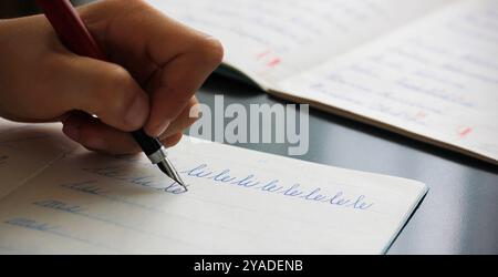 Darstellung einer linken Hand eines Kindes, die die Silben li und le mit einem Füllfederhalter in ein Copybook schreibt. Konzept zum Schreiben mit der linken Hand. Stockfoto