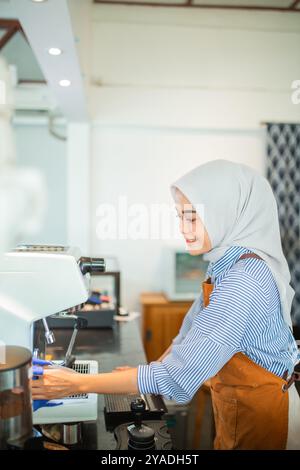 Indonesische Frau mit Hijab-Café-Arbeiter, der die Caféküche mit Lappen reinigt Stockfoto