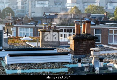 Rauch aus Schornsteinrohren auf dem Dach gewöhnlicher Einfamilienhäuser in den Niederlanden, Sonnenaufgang auf dem Dach des Stadtzentrums. Stockfoto
