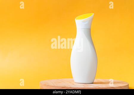 Eine elegante, moderne weiße Flasche mit gelbem Verschluss, die auf einer Holzoberfläche vor einem hellgelben Hintergrund platziert wird. Das Design ist minimalistisch und elegant, Stockfoto